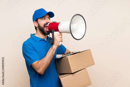 Delivery man with beard over isolated background shouting through a megaphone