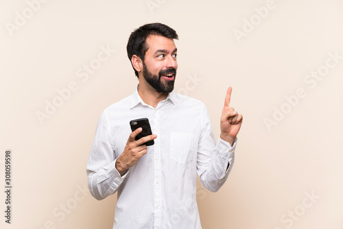 Young man with beard holding a mobile thinking an idea pointing the finger up