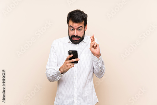 Young man with beard holding a mobile with fingers crossing and wishing the best