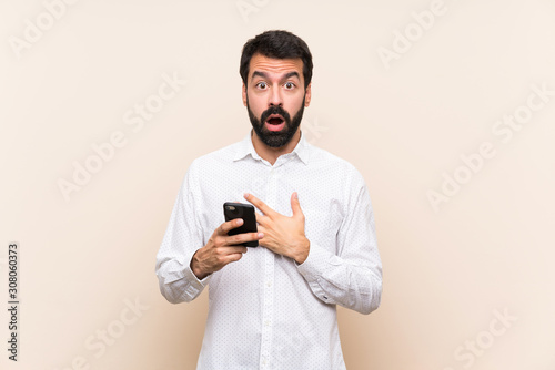 Young man with beard holding a mobile surprised and shocked while looking right © luismolinero