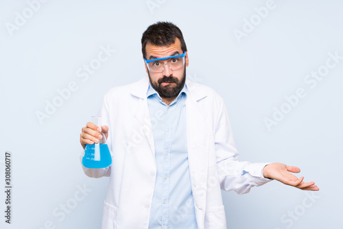 Young scientific holding laboratory flask over isolated background having doubts while raising hands