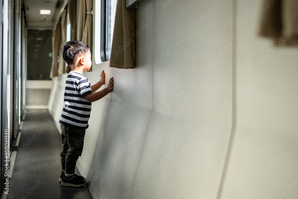 Side view of happy little boy oooking out through wide glass window of a train. Child traveling by railway.