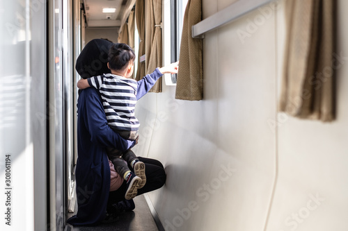 Happy young muslim mother waering hijan and little toddler boy looking out through window of a train, while it moving. Travel and family trip concept. photo