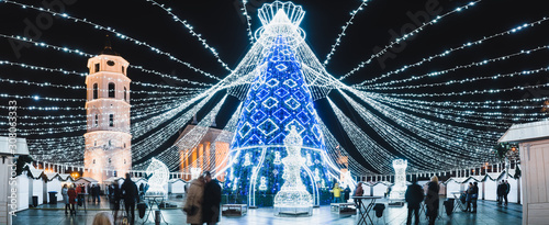 Vilnius, Lithuania, 2019: Beautiful Christmas tree decorated with white and blue lights chess queen for Christmas 2019 and New Year 2020, market and celebrations in Vilnius Cathedral square, panorama.