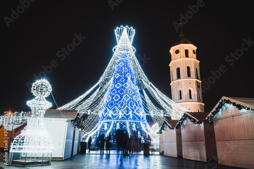 Vilnius, Lithuania, 2019: Beautiful Christmas tree decorated with white and blue lights chess queen for Christmas 2019 and New Year 2020, market and celebrations in Vilnius Cathedral square.