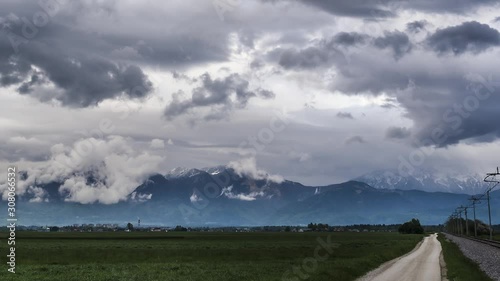 Time lapse summer storm clouds over Alps mountain range with grass field road and railroad in foreground photo