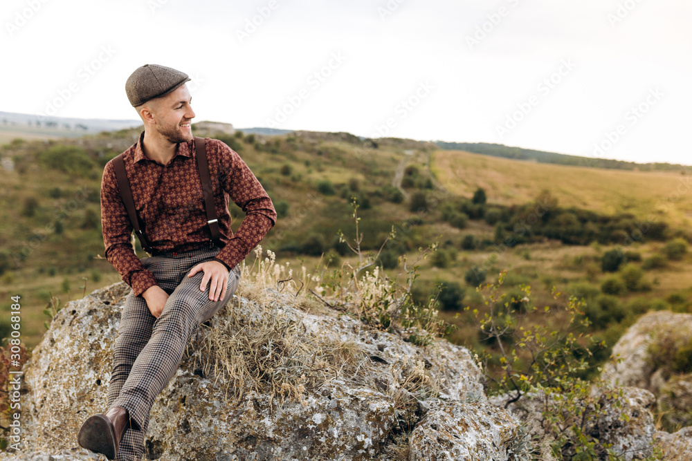 Image of a young farmer who stays on the top of the rock hill and looks into the distance to the beautiful landscape of own fields, thinking about future plans. Optimistic mood