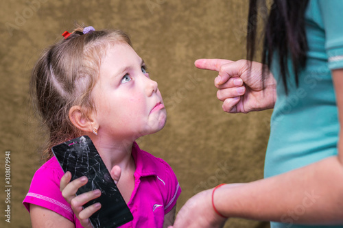 Mom punishes daughter for a broken phone. A little girl plaintively looks at parents.  The child accidentally broke the phone. The concept of children's raise photo