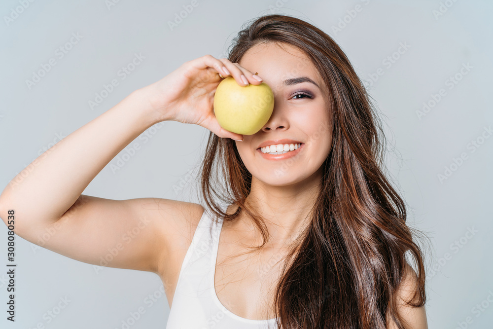 Beauty portrait of smiling young asian woman girl holding green apple near clean face on grey background