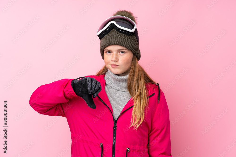 Ukrainian teenager skier girl with snowboarding glasses over isolated pink background showing thumb down sign