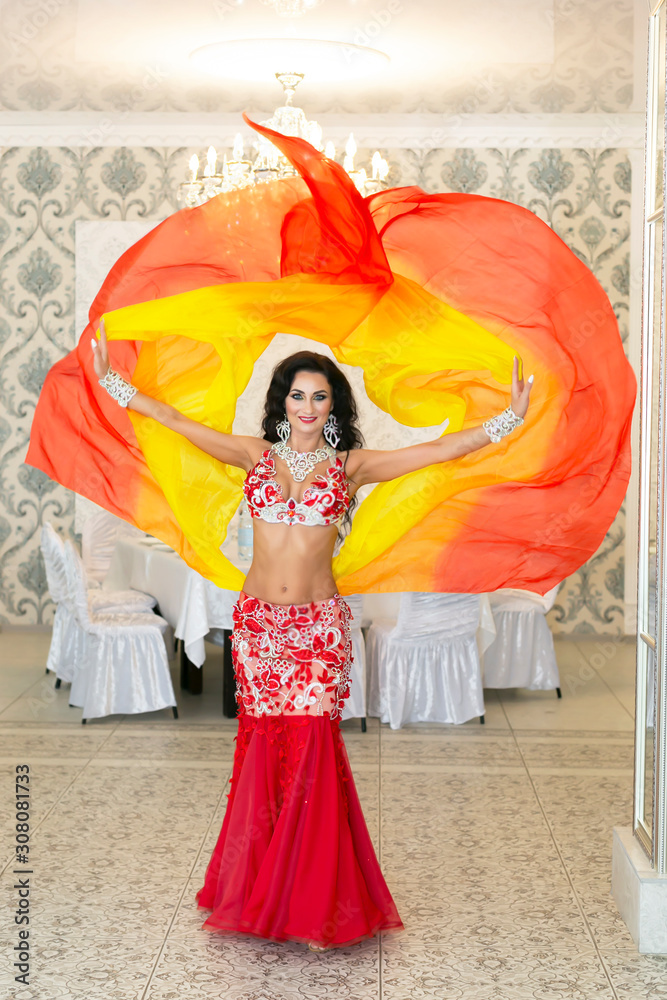 Oriental dancer in a red-yellow dress. Belly dancer throws ends of her beautiful  orange skirt into the air. Stock Photo