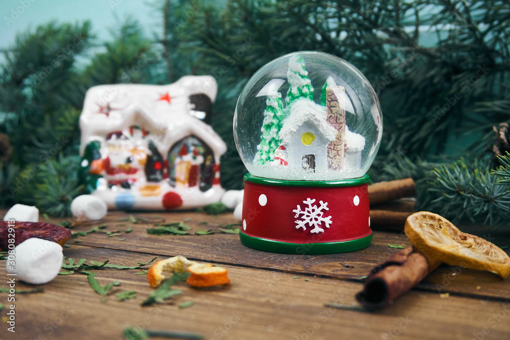 glass snow globe with birds inside on the background of fir branches and Christmas tree toys. cinnamon and orange sticks. winter fairy tale