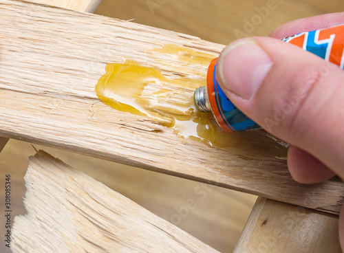 Furniture repair at home. Carpenter applies glue to a wooden cracked board. Close-up, selective focus.