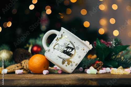 Christmas glass standing sideways on a tangerine. Staka n Skakao and marshmallows. Christmas background of a Christmas tree with toys and lights. photo