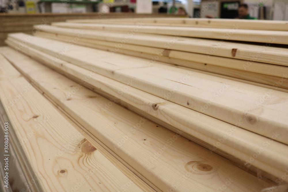 View of the beginning of the folded planed boards in the construction store. Behind them are silhouettes of people. Shot under shop lighting.