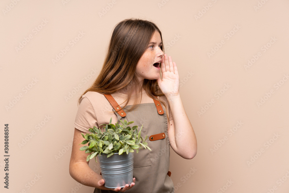Ukrainian teenager gardener girl holding a plant shouting with mouth wide open Ukrainian teenager gardener girl holding a plant shouting with mouth wide open