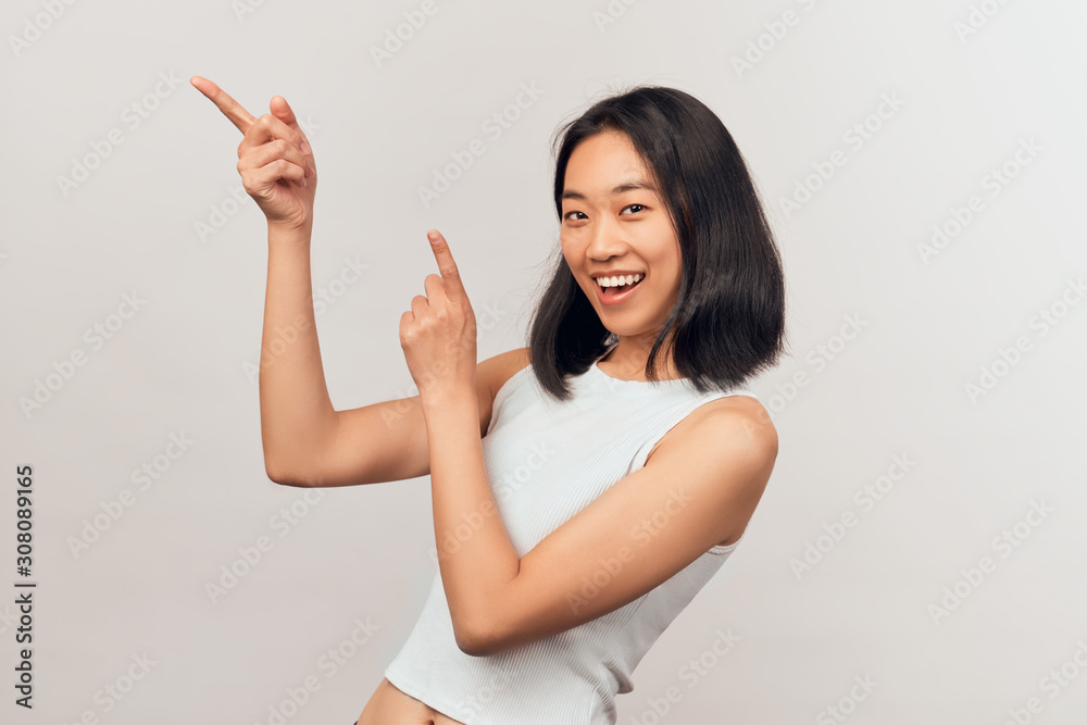 Portrait with copy space of charming brunette pointing forefinger on empty place, looking at camera. Businesslike young woman Asian appearance dressed in short shirt stands isolated white background Portrait with copy space of charming brunette pointing forefinger on empty place, looking at camera. Businesslike young woman Asian appearance dressed in short shirt stands isolated white background