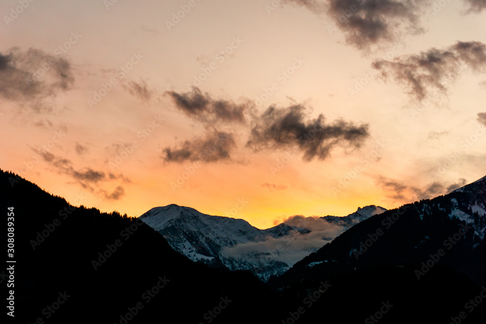 colorful winter sunset over snowy mountain landscape with dark foreground