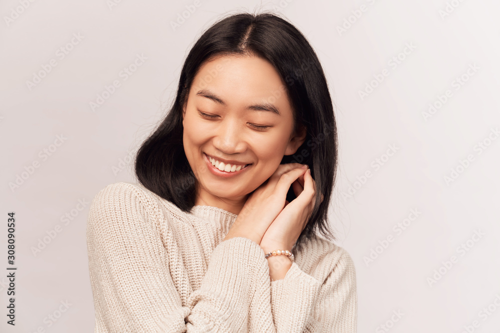 Calm brunette female with closed eyes, keeps both palms on heart, feels gratitude. young woman Asian appearance dressed in knitted warm sweater stands isolated white background in Studio. Calm brunette female with closed eyes, keeps both palms on heart, feels gratitude. young woman Asian appearance dressed in knitted warm sweater stands isolated white background in Studio.
