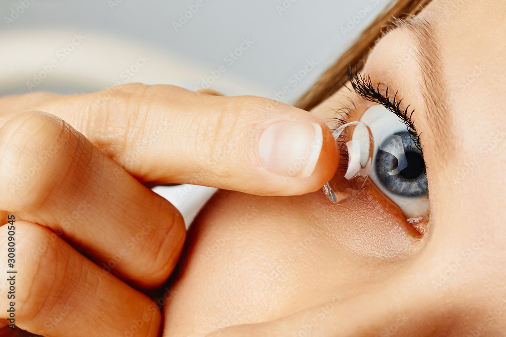 Fototapeta premium Young woman puts contact lens in her eye. Eyewear, eyesight and vision, eye care and health, ophthalmology and optometry concept
