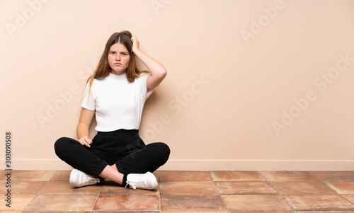 Ukrainian teenager girl sitting on the floor with an expression of frustration and not understanding © luismolinero