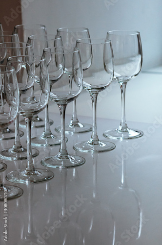 A raw of empty wine glasses on the table. Many transparent high stalk glasses on the table next to window, beautiful reflections, natural light. Catering, holiday, cafe, restaurant glassware