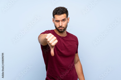 Handsome man over isolated blue background showing thumb down with negative expression