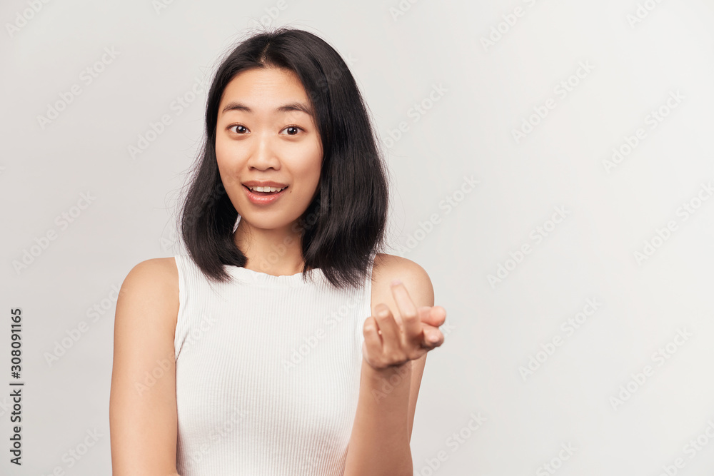Smiling positive young female points at camera with index finger, expresses choice. Businesslike young woman Asian appearance dressed in short shirt stands isolated white background in Studio. Smiling positive young female points at camera with index finger, expresses choice. Businesslike young woman Asian appearance dressed in short shirt stands isolated white background in Studio.
