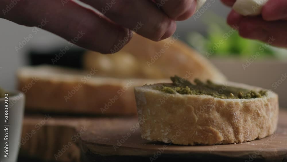 Slow motion closeup man hands making bruschetta with pesto and mozzarella Slow motion closeup man hands making bruschetta with pesto and mozzarella