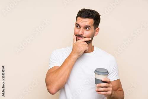 Young man with beard holding a take away coffee over isolated blue background thinking an idea