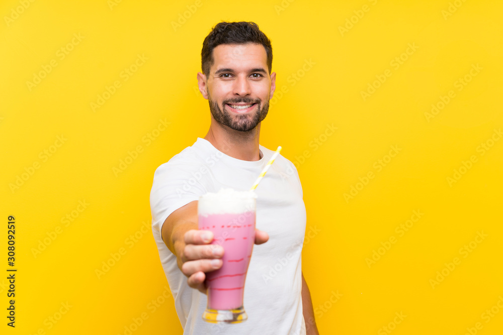 Young man with strawberry milkshake over isolated yellow background Young man with strawberry milkshake over isolated yellow background