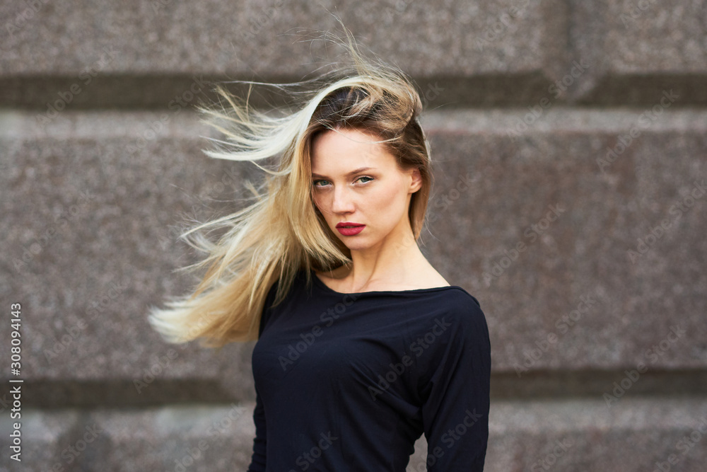 Sexy blonde girl in a black dress. With flying hair against a stone wall.