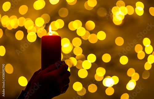 A woman is holding a red candle in her hands. In the background, lights with festive bokeh light up. Concept: festive illumination