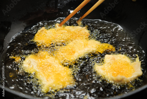 gold color meat in boiling oil on black