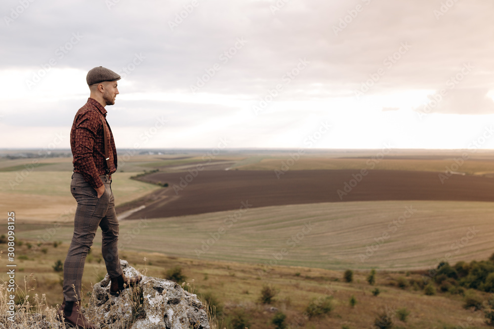 Pensive businessman, farmer in suit looking away, hands in pockets. Standing on outdoor on the top of hill. Fields and hill background. Man thinking about chalenges and strategy