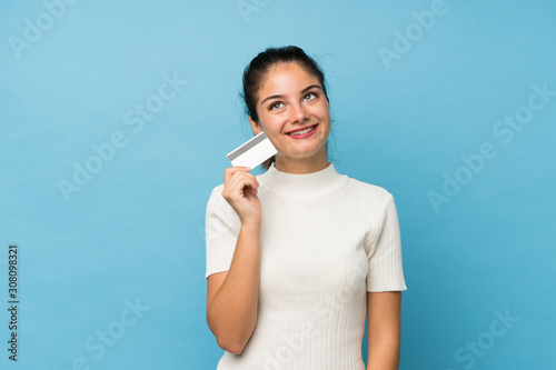 Young brunette girl over isolated blue background holding a credit card