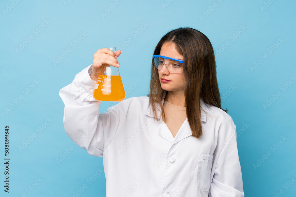 Young brunette girl over isolated blue background with a scientific test tube Young brunette girl over isolated blue background with a scientific test tube