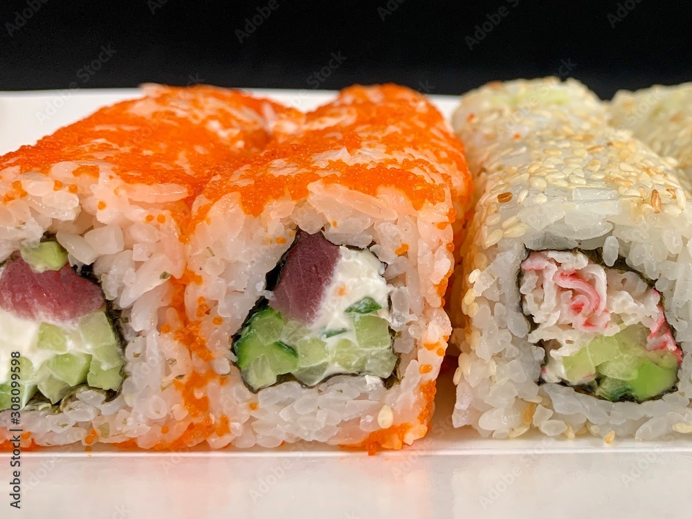 Sushi with red fish and avocado, close-up, on a black background. Japanese traditional cuisine, delicious sushi with dill and sesame seeds. Rolls - California and Philadelphia. Sushi with red fish and avocado, close-up, on a black background. Japanese traditional cuisine, delicious sushi with dill and sesame seeds. Rolls - California and Philadelphia.