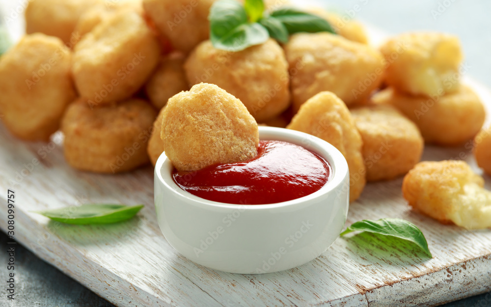 Fried mozzarella, cheddar cheese bites, balls with ketchup on white wooden board