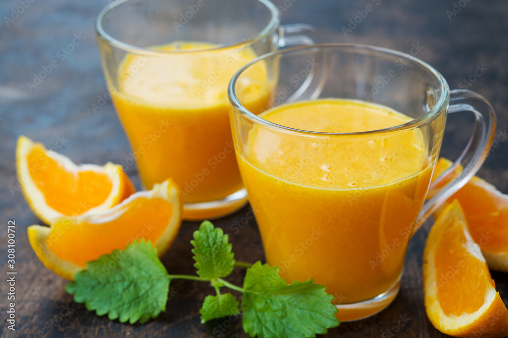 Close up two glass mugs of freshly squeezed orange juice stand on a wooden background. Horizontal orientation. Close up two glass mugs of freshly squeezed orange juice stand on a wooden background. Horizontal orientation.