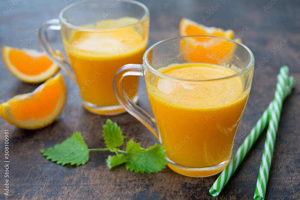 Two glass mugs of freshly squeezed orange juice stand on a wooden background. Horizontal orientation. Two glass mugs of freshly squeezed orange juice stand on a wooden background. Horizontal orientation.
