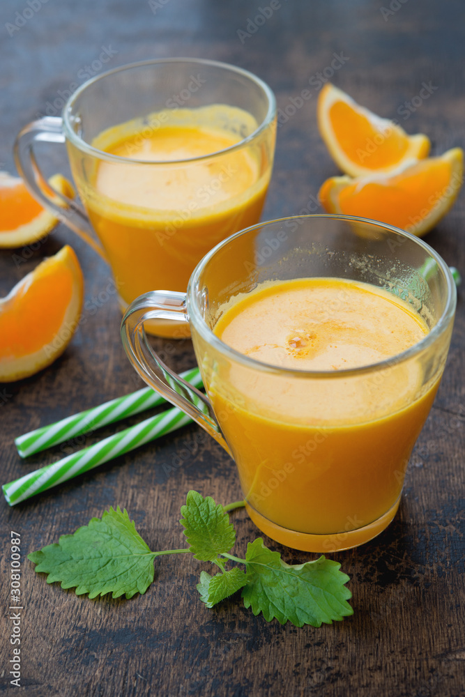 Two glass mugs of freshly squeezed orange juice stand on a wooden background. Horizontal orientation. Two glass mugs of freshly squeezed orange juice stand on a wooden background. Horizontal orientation.