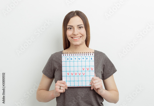 A smiling woman holds a calendar with marked days. The concept of the menstrual period.