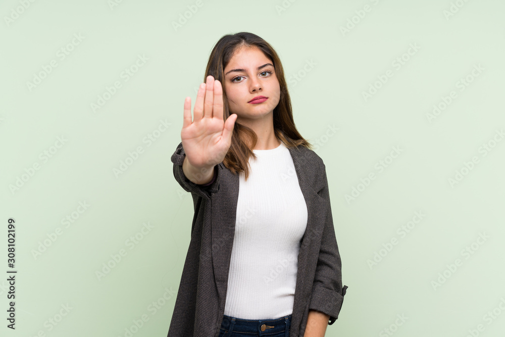 Young brunette girl with blazer over isolated green background making stop gesture Young brunette girl with blazer over isolated green background making stop gesture