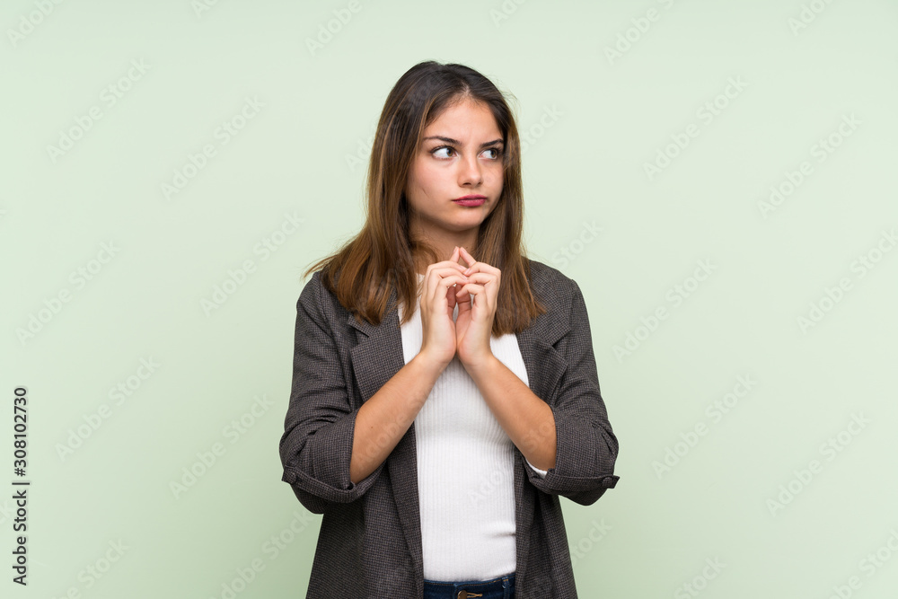 Young brunette girl with blazer over isolated green background scheming something Young brunette girl with blazer over isolated green background scheming something