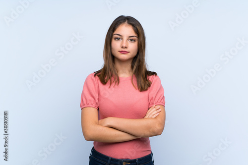 Young brunette girl over isolated blue background keeping arms crossed