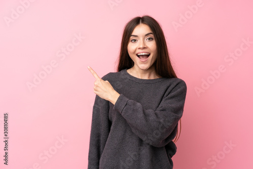 Young woman over isolated pink background surprised and pointing side