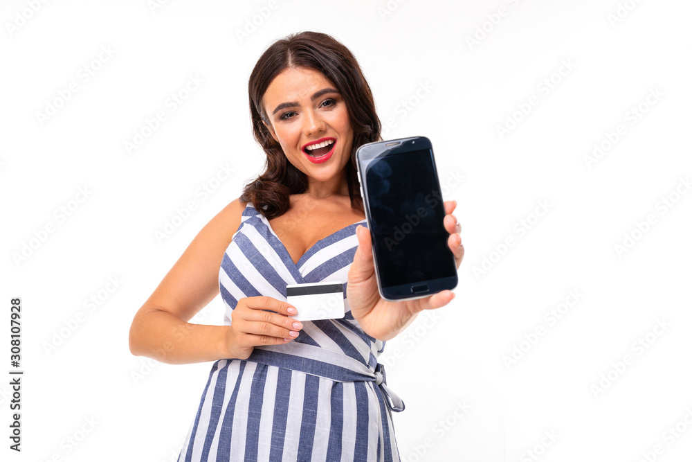 attractive brunette girl in a striped dress with a neckline with a smartphone with mockup and credit card in her hands on a white background attractive brunette girl in a striped dress with a neckline with a smartphone with mockup and credit card in her hands on a white background