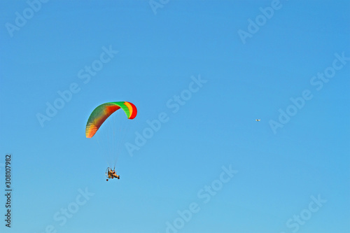 paramotor with paraglider pilot on blue sky, motor hang glide tricycle with colorful sail, extreme sport diversirty