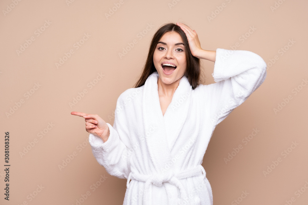 Young girl in a bathrobe over isolated background surprised and pointing finger to the side
